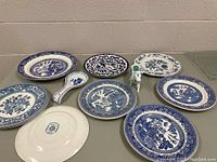 Top down view of the 10 blue and white plates and cow creamer arranged on table showing varied patterns and styles.