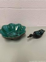 Photo showing both the green glazed flower-shaped bowl and the duck figurine together on a table against a wall.