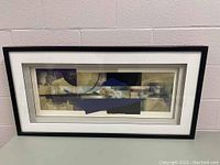 Framed abstract artwork with geometric shapes in a black frame and white matting.