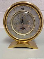 Front view of Bulova Millennia moon phase desk clock with solid brass frame and base, showing clock face, subdials, and moonphase display.