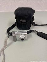 Silver Canon PowerShot A700 camera in front of black camera case on white surface.