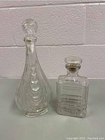 Two clear glass decanters, one tall with swirl texture, one rectangular with geometric etched patterns