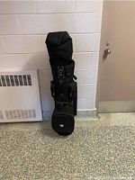 Full view of the black golf bag standing upright against a wall showing its size and compartments