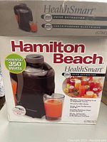 Box showing Hamilton Beach HealthSmart 67815C Juice Extractor product details and branding with a glass of juice image.