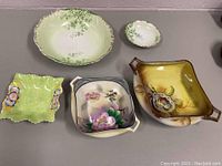 Lot of five decorative porcelain and glass dishes arranged on a table surface, showing various shapes and floral designs.