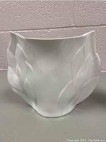 Close-up side view of white porcelain vase with leaf motif and flared irregular rim.