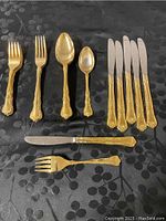 Image showing several pieces of flatware including forks, spoons, and knives with gold plated handles arranged on a dark patterned cloth.