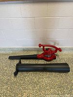 Full side view of the red Toro leaf blower main unit with two black nozzle attachments placed separately on surface