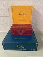 Three stacked Trivial Pursuit board game boxes: yellow Genius Edition box on top, red Baby Boomer Edition box in middle, blue Master Game Genius II Edition box on bottom.