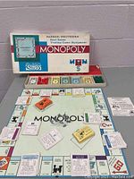 Vintage 1961 Monopoly game board laid out with cards, money, houses, hotels, and metal player tokens visible, along with the original box showing Parker Brothers branding.