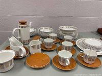 Full view of the Ridgway ironstone set showing coffee pot, creamer, sugar bowl, gravy boat, and orange saucers with teacups and dinnerware stacks