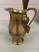 Vintage brass water pitcher showing the wide spout, curved handle, and floral engraving