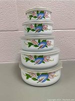 Stacked view of five nesting vintage porcelain enamel bowls with lids showing floral decoration.