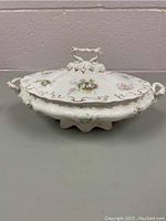 Side view of the vintage porcelain tureen showing floral design, ornate handles, and decorative gold accents on lid and body.