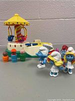 Overview of vintage Fisher Price Little People carousel toy with figures and four Smurf figurines in front.
