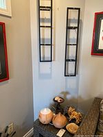 Photo of two black metal wall hangings mounted on wall above a corner table with two round wooden atomizers, metal stand with polished rock eggs, dried flowers, and wooden bowl.