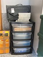 Plastic storage drawer organizer with several clear plastic bins and a gray zippered bag on top
