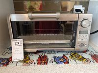 Front view of Breville BOV450XL toaster oven on countertop showing stainless steel finish and size values on note card.