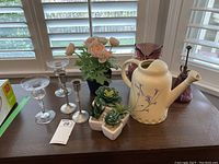 Photo showing candlestick holders, faux plants in pots, watering can, owl vase, and plant mister on window sill