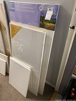 Six blank canvases leaning against the wall, with the largest canvas packaged and marked 24 x 48 inches.