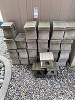Stack of 26 cement garden bricks arranged in multiple rows against an exterior wall on a gravel base.