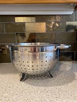 Photo of stainless steel metal colander with handles and feet on kitchen counter