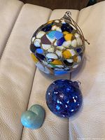 Overview shot showing all three items: large multicolored glass ball, smaller blue and white glass ball, and baby blue stone heart on a beige surface.