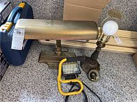 Photo showing three lamps: a vintage bankers lamp with brass finish, a small ornate lamp with white bulb, and an outdoor work light with yellow frame.