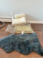 Overview of linens stacked on floor and blue-gray lambskin rug beside them on wooden floor