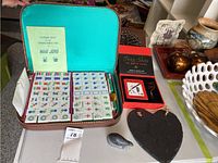 Open mahjong case showing tiles and instruction booklet, Feng Shui book, red box crystal set and stone heart hanging with soapstone seal carving on the table