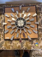 Front view of the sunburst style wall clock with mirrored trapezoidal pieces arranged radially around a black and silver center clock face.