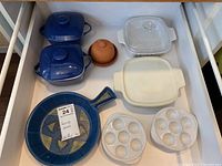 Photo showing variety of serving dishes including blue ceramic covered dishes, terra cotta cloche, CorningWare and glass bakeware, egg plates, and a blue ceramic skillet.