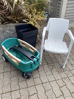 Photo showing the green Little Tikes wagon, white plastic garden chair, and tall black plastic garden planter placed on a paved patio area.