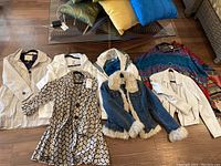 Full view of six women's coats laid out on wood floor, showcasing variety of colors and styles