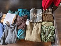 Overview of 8 women's sweaters in various colors and styles folded on a dark surface.