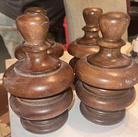 Close-up photo showing four wooden bannister tops with rounded, turned shapes and a brown finish.