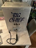Photo of the Big Chief Electric Smoker showing front side with branding, power cord, and handle on a table.