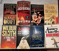 Top-down photo of eight used paperback books arranged in two rows of four, showing titles and authors clearly.