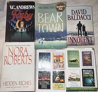 Photo showing front covers of 9 fiction books from different authors laid out on a white fabric surface.