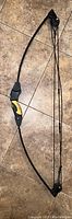 Full view of the black and yellow recurve bow with string and pulleys on a tiled floor