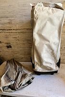 Beige colored carry bag standing upright with a zippered closure and a handle next to a folded inflatable mattress component of the bed set.