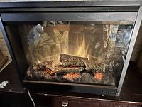Front view of the electric fireplace insert showing the black metal frame, glass front, and simulated logs with flame effects inside.