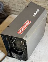 Grey rectangular Craftsman 1/2 HP garage door motor housing with wiring and internal components partially visible; shows signs of heavy use.