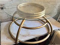 Full view of round glass coffee table with gold circular metal base on a white folding table, showing structure and condition of glass top and metal base.
