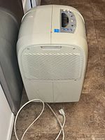 Side angle view of beige Kenmore dehumidifier with power cord on tiled floor.