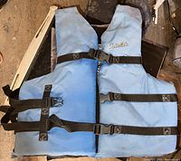 Front view of a blue Cabela's life jacket with three black adjustable straps and buckles horizontally across the front.