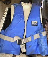 Blue and off-white Mustang Survival life jacket showing front side with straps and buckle.
