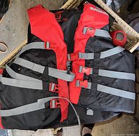 Two black and red Outbound life jackets with gray adjustable straps and red buckles laid side by side