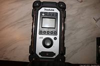 Top view showing the Makita jobsite radio's digital display, control buttons, volume knob, and rugged protective bumpers