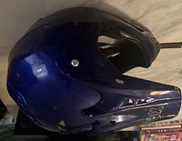 Side view of used blue motocross helmet showing scuffs and wear marks.